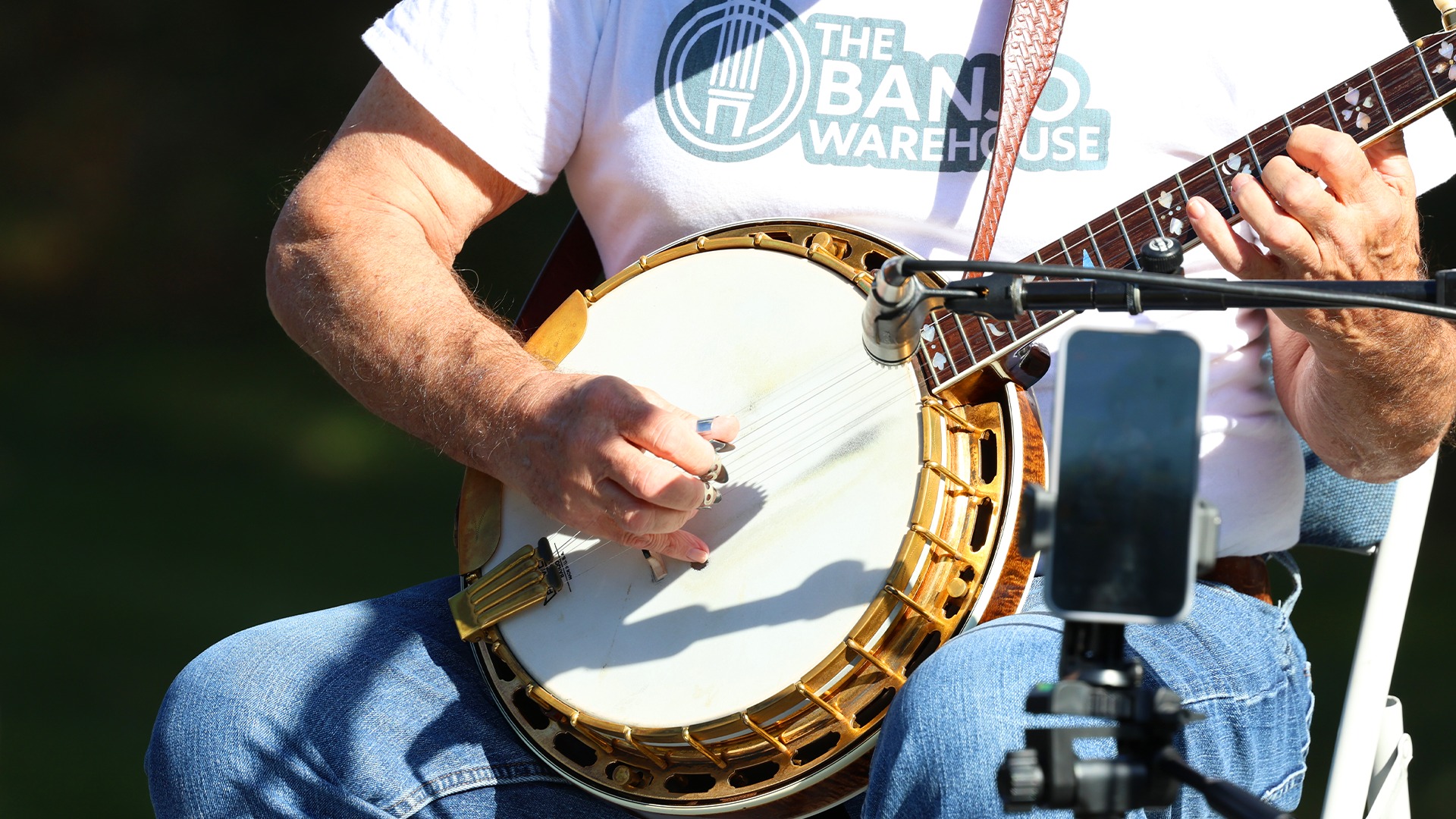 Geoff Hohwald wearing The Banjo Warehouse t-shirt while playing a gold-tone banjo at outdoor performance in Yellow Springs, Ohio