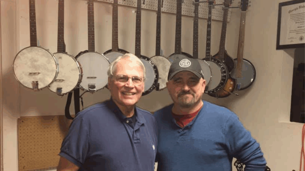 Geoff Hohwald at Banjo Warehouse in Yellow Springs, Ohio with vintage and professional banjos displayed on wall behind him
