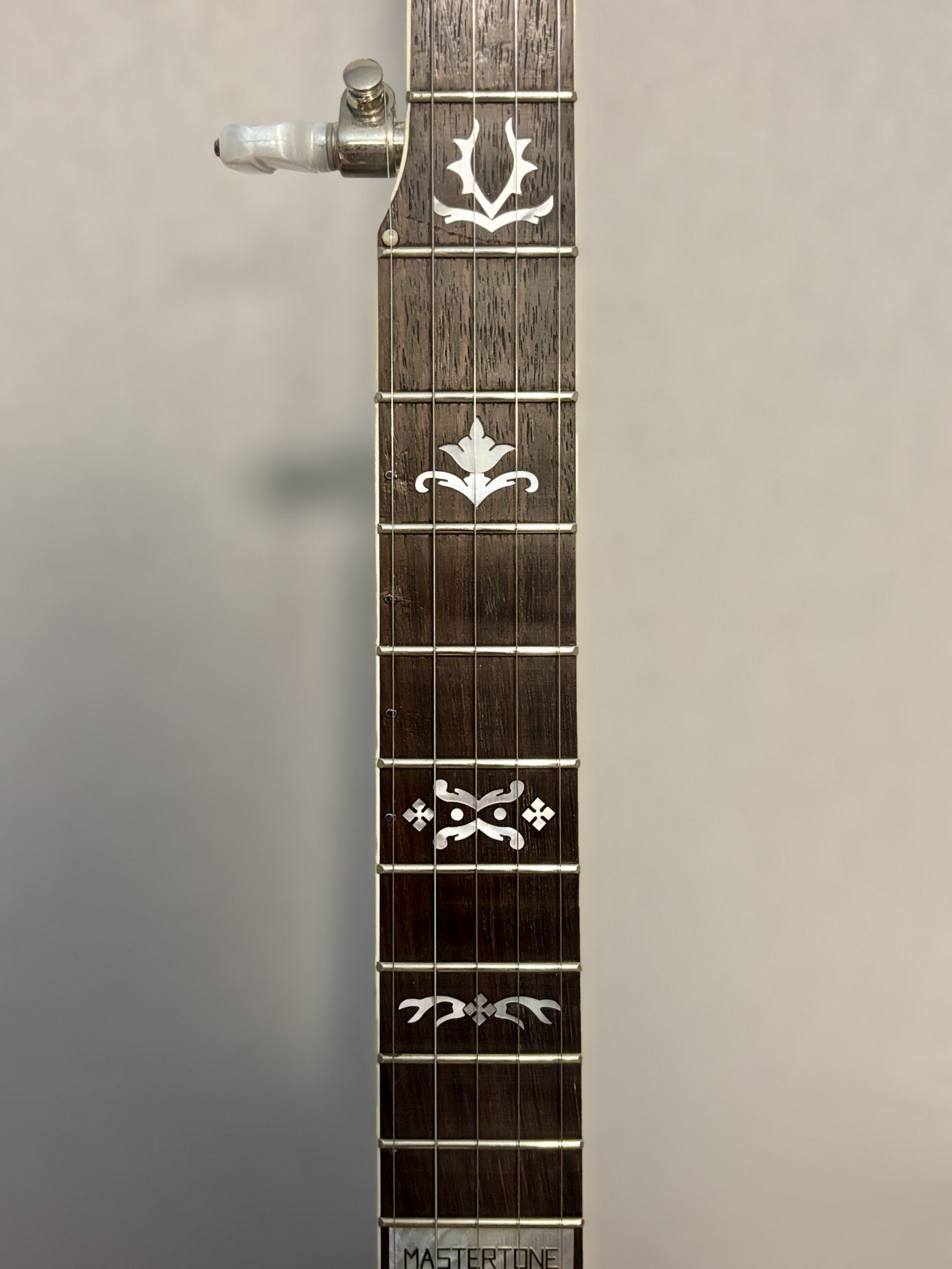 Mid-section of Gibson RB-3 fretboard showing tulip, fleur-de-lis, and ornate wreath inlays in pearl on rosewood, with Mastertone block visible at bottom