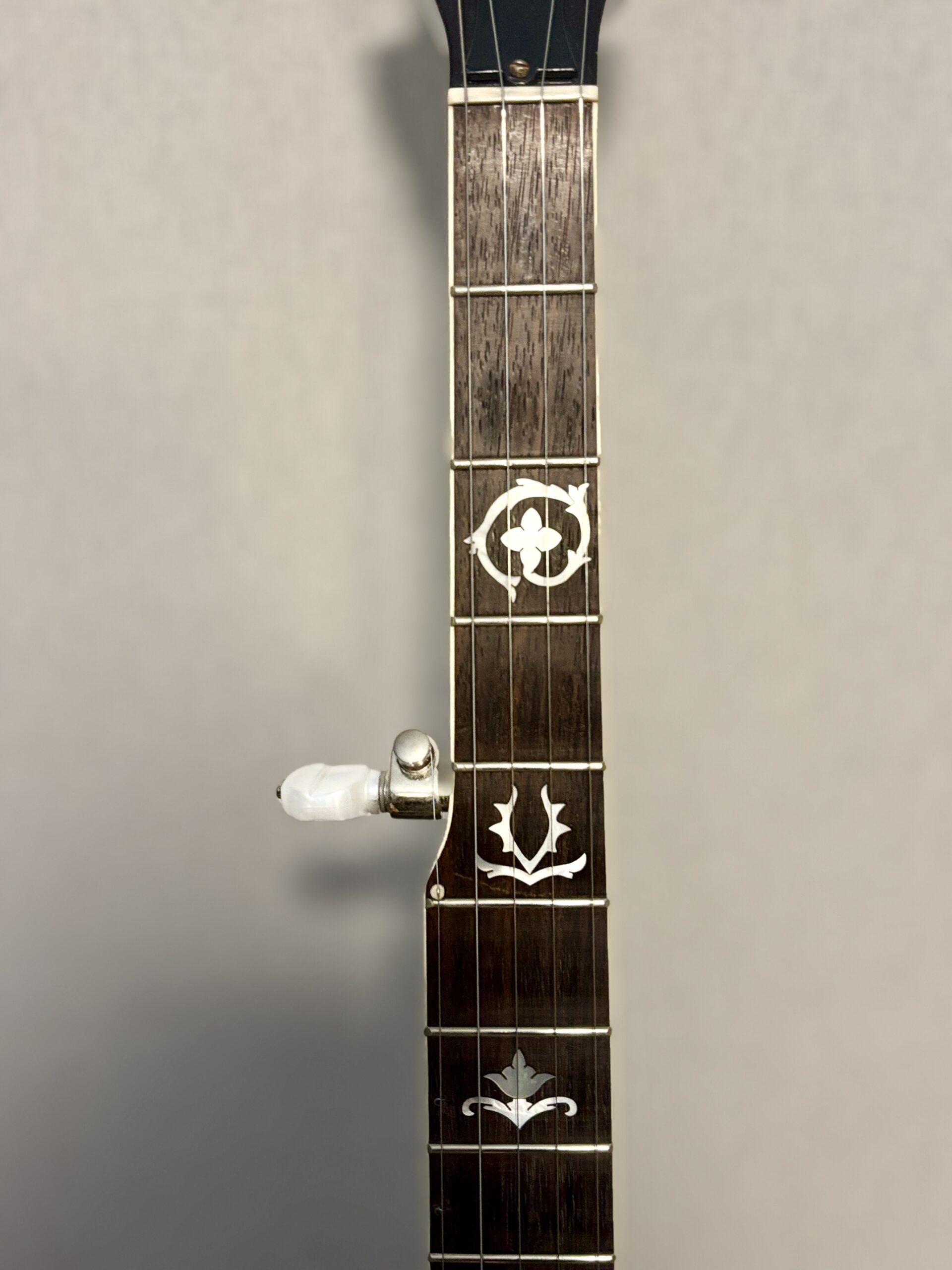 Upper frets of Gibson RB-3 showing wreath inlay pattern including four-leaf clover surrounded by wreath at 3rd fret and tulip design at 5th fret, with tuner visible