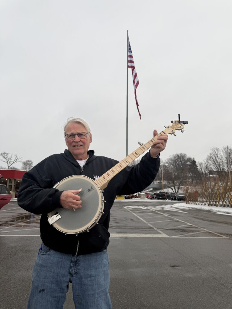 Geoff Hohwald owner of Banjo Warehouse holding a Deering Goodtime openback banjo in front of the largest American flag in the state of Ohio in Zanesville