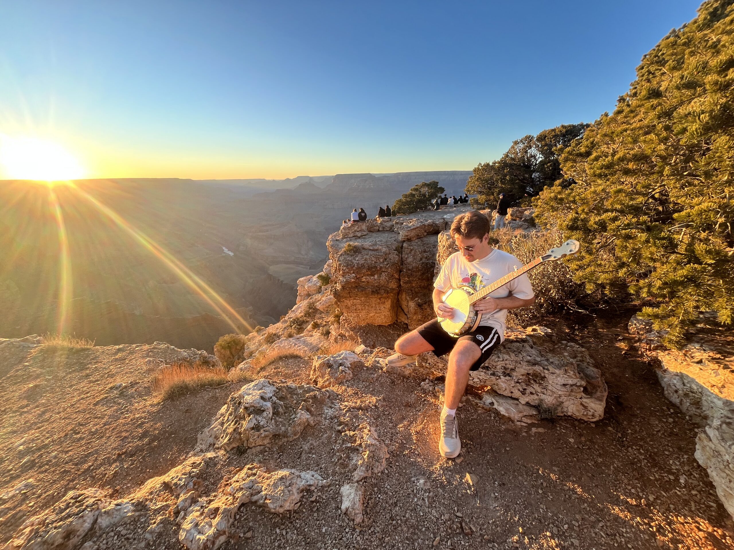 Gold Tone CC-100R banjo leaning on cliff edge at Grand Canyon with wide canyon panorama and orange sky at sunrise