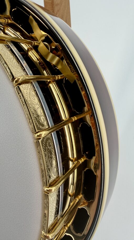 Close-up of the hand-engraved brass tension hoop on the Gold Tone Custom Shop OB-2 JM Joe Mullins banjo, showing floral and sunburst engraving, gold-plated hooks, and sunburst resonator — exclusive to Banjo Warehouse